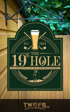 Lade das Bild in den Galerie-Viewer, Green sign with 'The 19th Hole' logo featuring a beer glass and golf elements, hanging on a building.