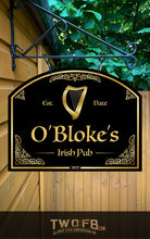 Load image into Gallery viewer, Sign for O&#39;Bloke&#39;s Irish Pub with a harp symbol, hanging against a wooden wall with greenery.
