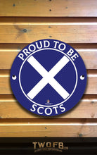 Load image into Gallery viewer, Round blue sign with white cross and text &#39;Proud to be Scots&#39; on a wooden background
